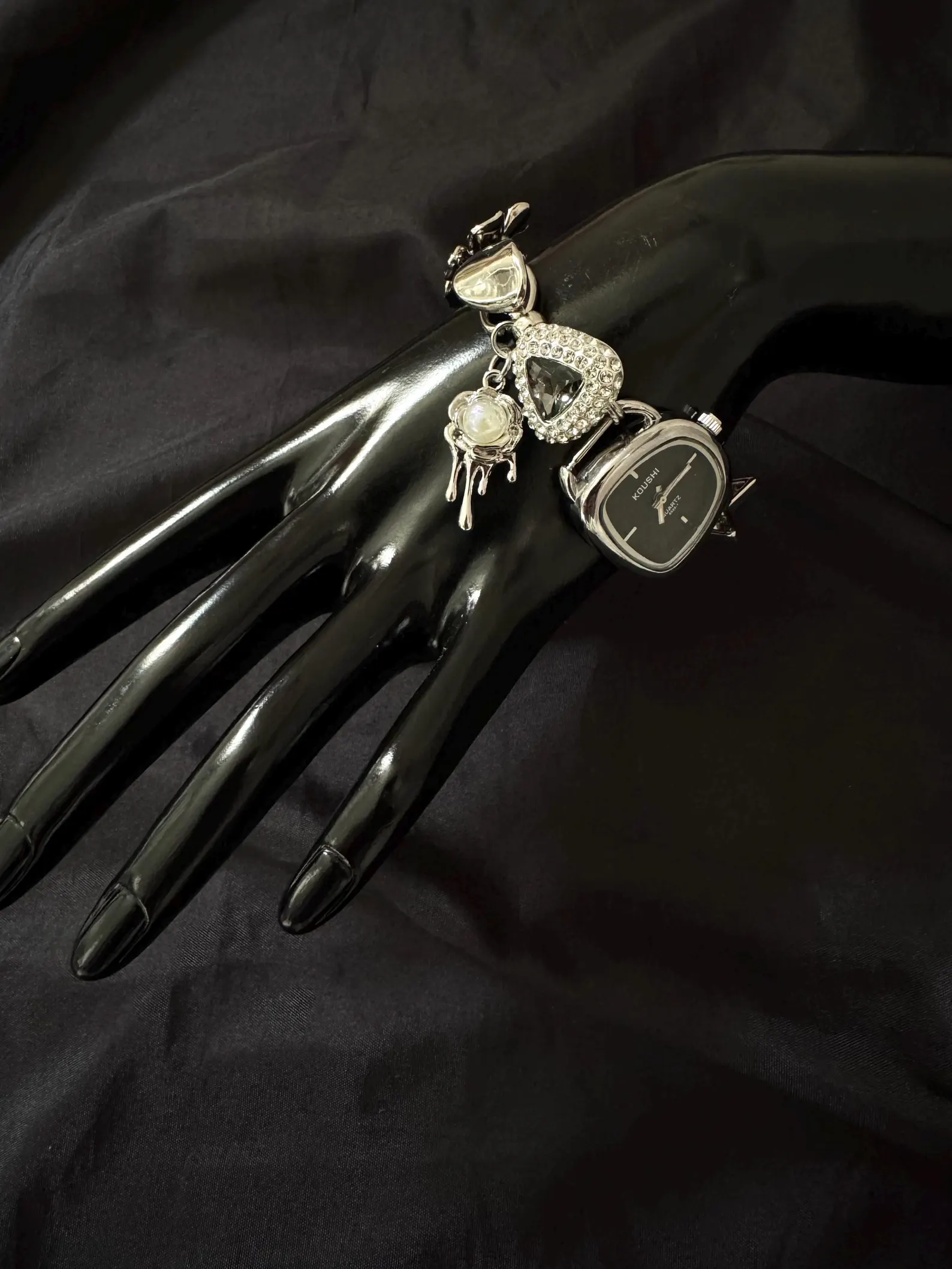 Mechanical-style bracelet watch focused on charm deployment and button-led fastening